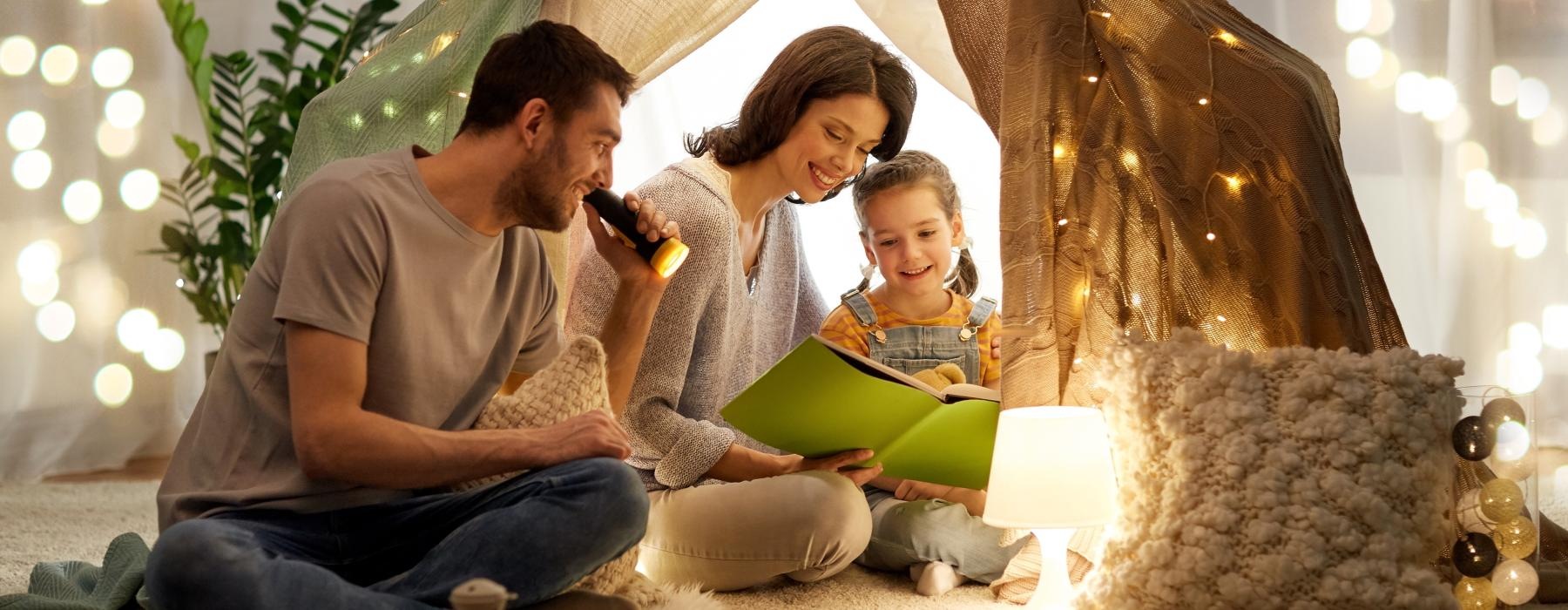 young family reads together under a tent in their living room